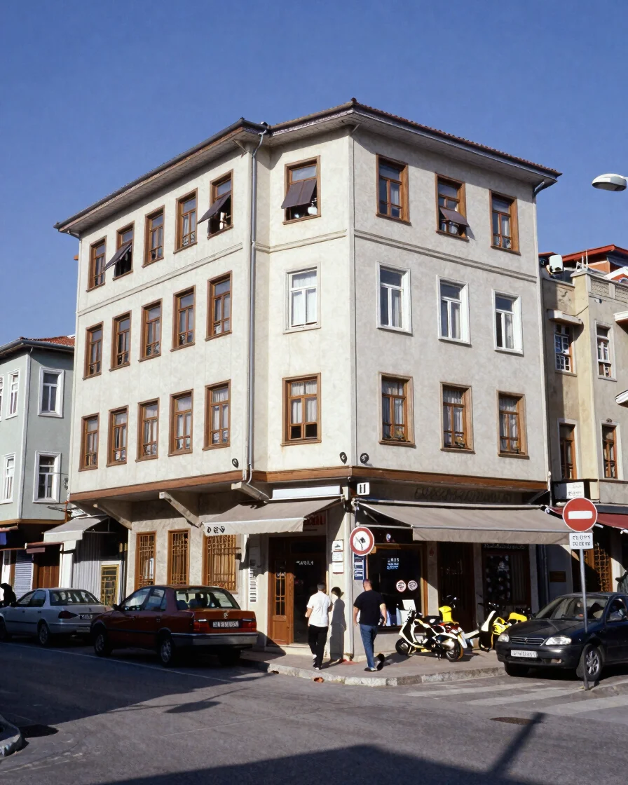 Ümraniye’de sıradan bir apartman cephesi ve yakınındaki küçük bir mahalle iş yeri, gündelik şehir ışığı altında, geniş ç